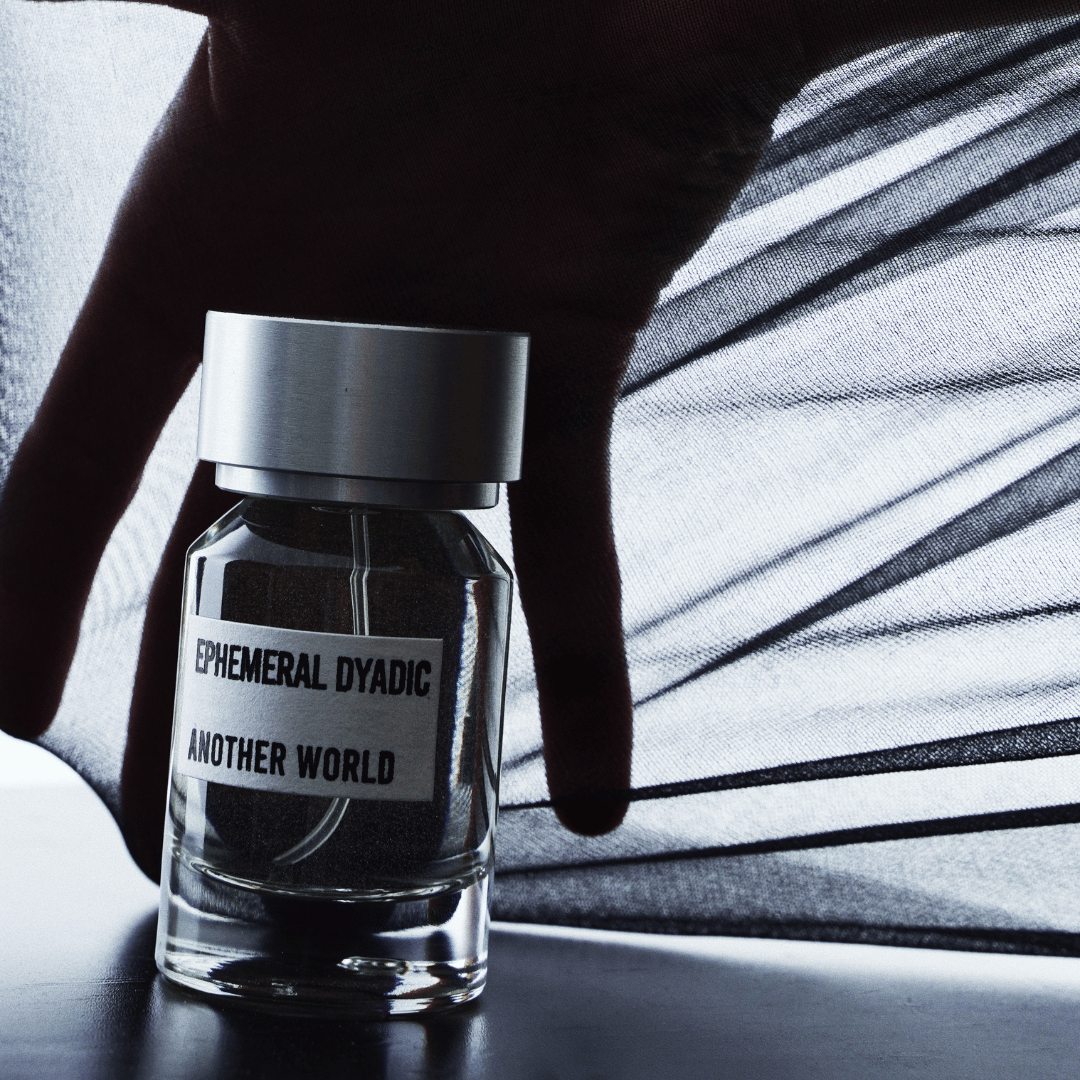 dunkle Hand mit einem Schleier und einem Parfum Flakon mit Metallkappe davor