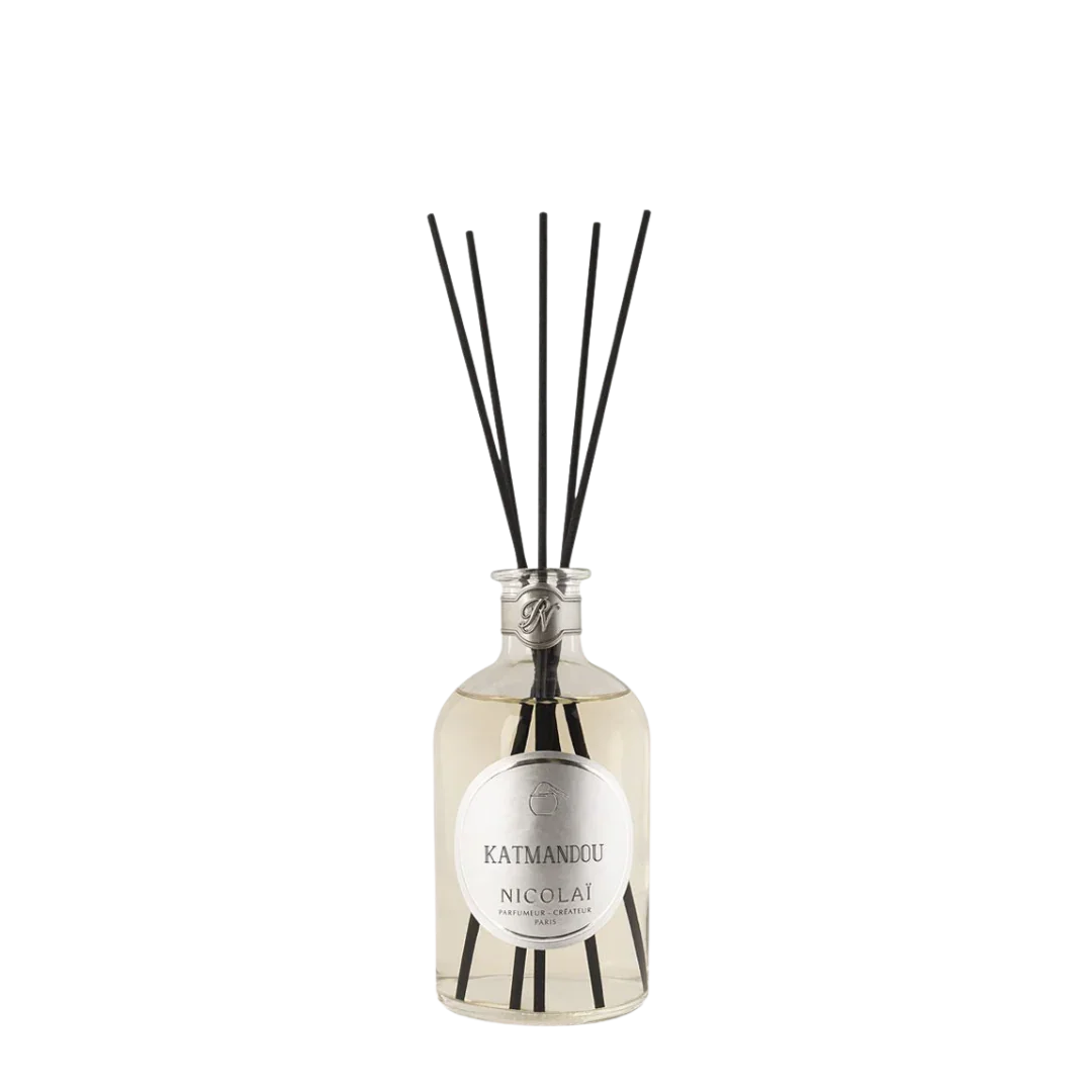 Diffuser "Katmandou" von Nicolaï, präsentiert in einer klaren Glasflasche mit schwarzem Verschluss und schwarzen Duftstäbchen.