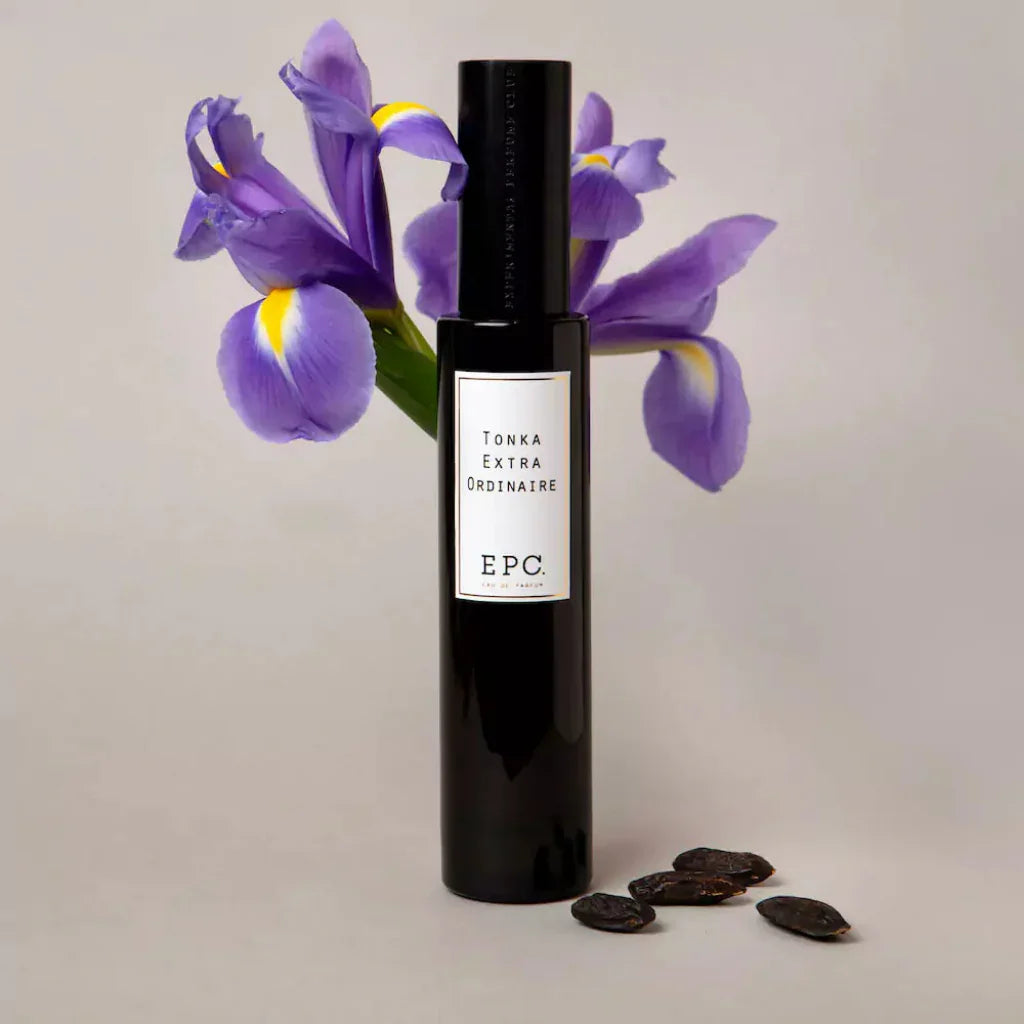 Dunkle Parfümflasche „Tonka Extraordinaire“ von Experimental Perfume Club, flankiert von Irisblüten und Tonkabohnen.