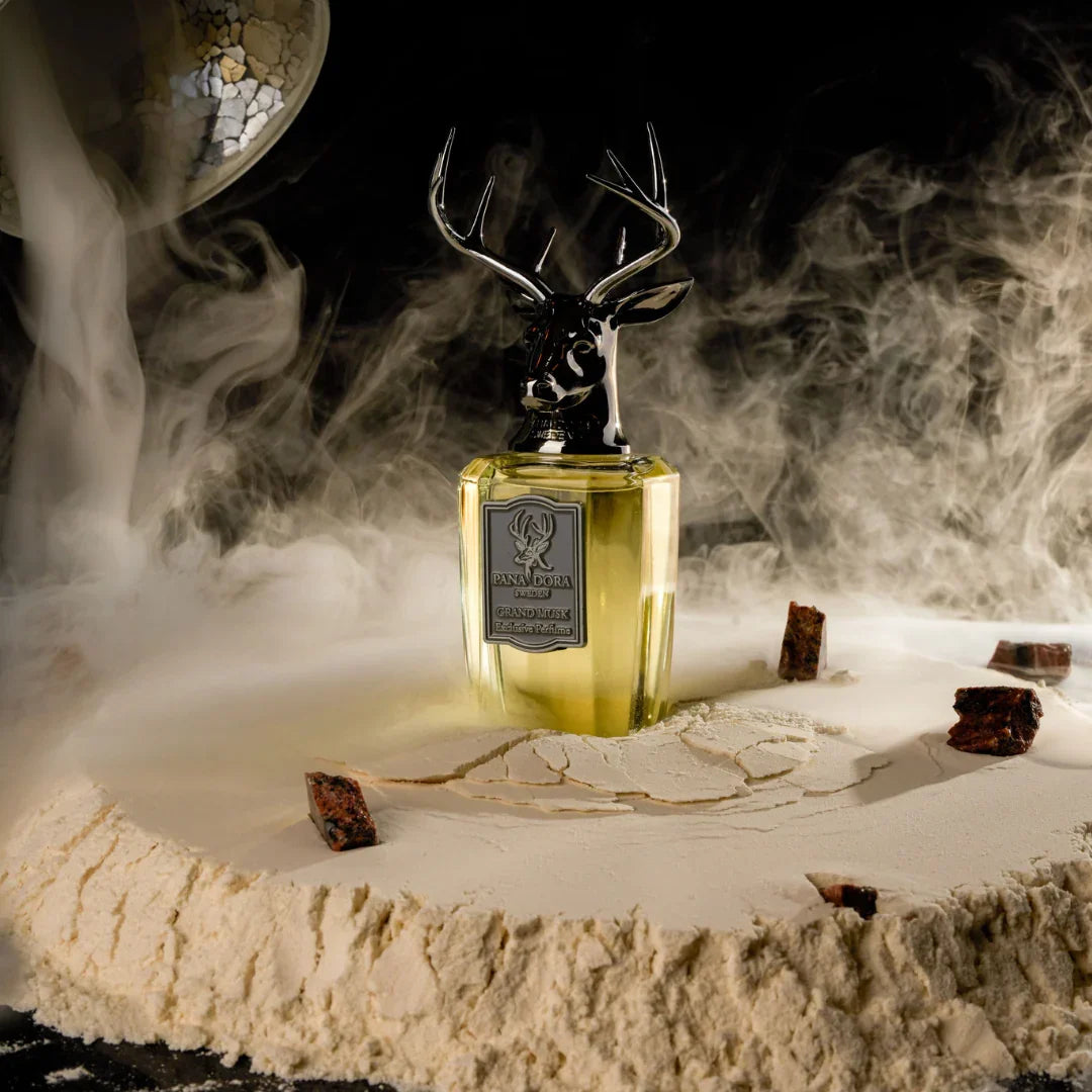 Parfümflakon "Grand Musk" von "Pana Dora" mit Hirschkopf-Verschluss, umgeben von Nebel auf einer staubigen Fläche.