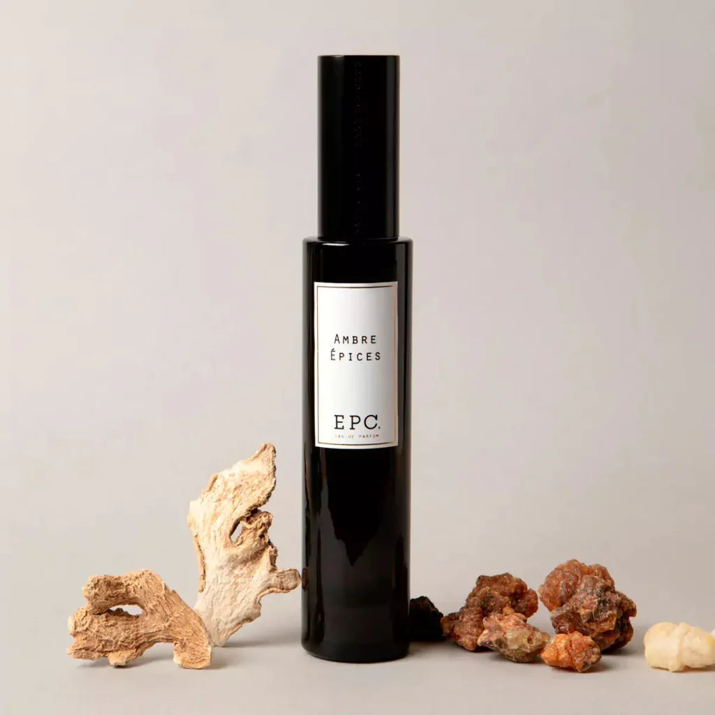 Dunkle Glasflasche "Ambre Epices" von Experimental Perfume Club steht umgeben von verschiedenen Harzbrocken.
