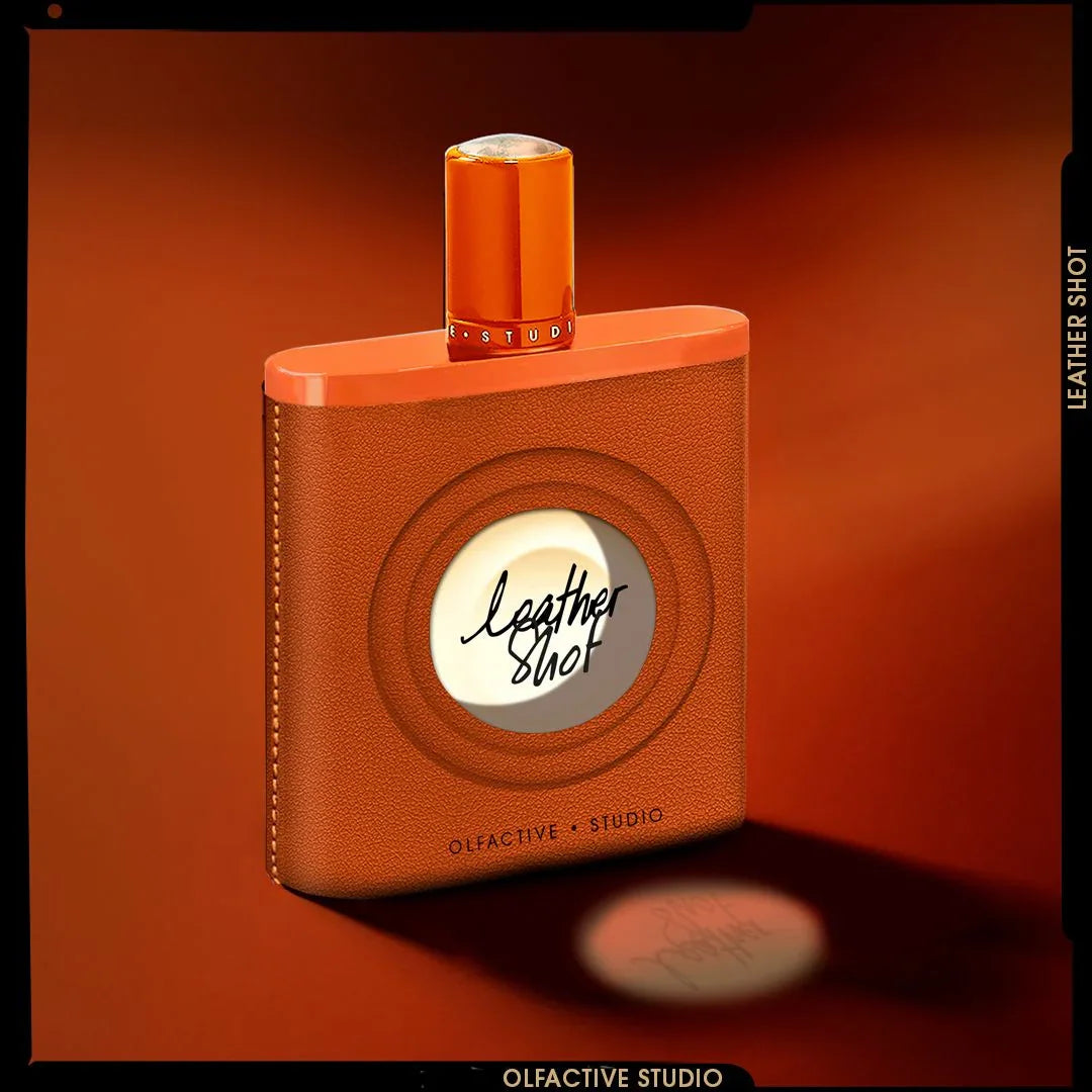 Parfumflakon "Leather Shot" von Olfactive Studio mit brauner Lederoptik, runder Sichtfenster und orangenem Verschluss.