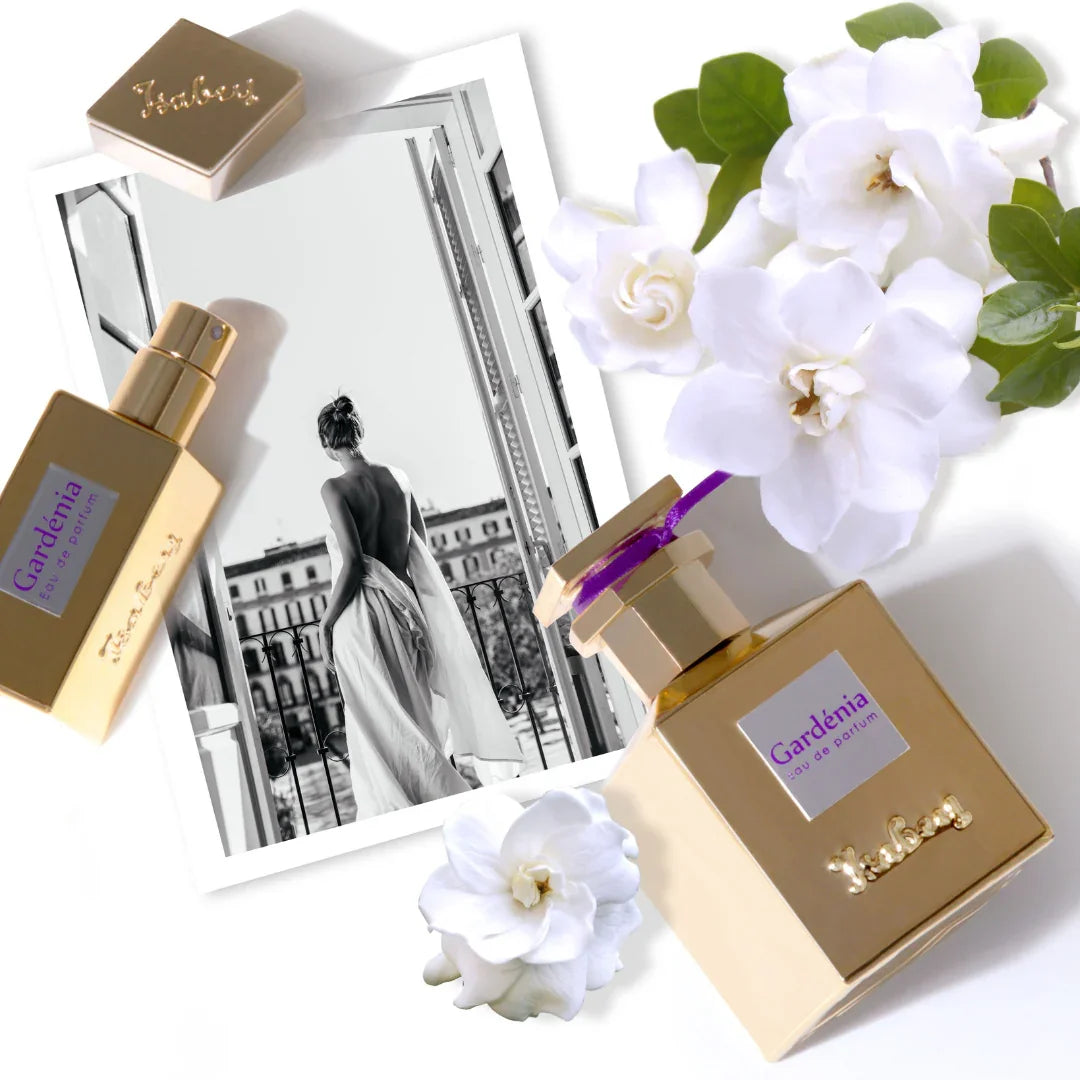 Parfümflasche „Gardenia“ von Isabey mit blumigem Design, goldene Kappe und lilafarbenes Etikett, daneben weiße Blumen.