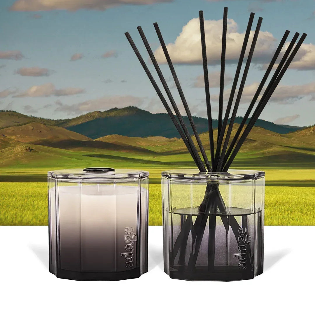 Zwei Duftkerzen in Glasbehältern von "source adage" mit dem Titel "Great Plains Duftkerze". Ein Behälter enthält schwarze Duftstäbchen. Die Gläser sind transparent mit einem Farbverlauf von weiß zu schwarz.