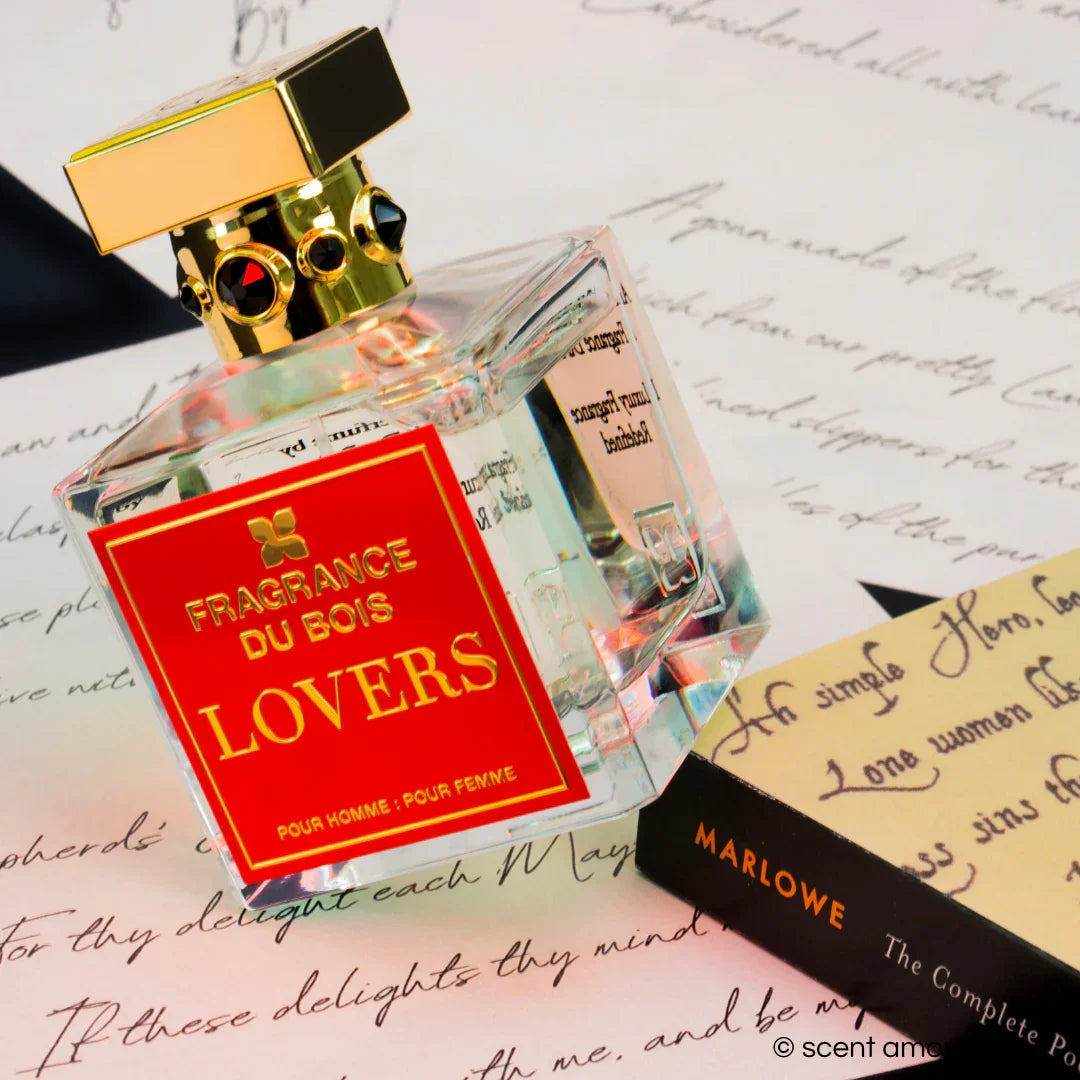Klares Parfümflakon mit goldener Kappe und rotem Etikett "FRAGRANCE DU BOIS LOVERS" auf einem handschriftlichen Hintergrund.