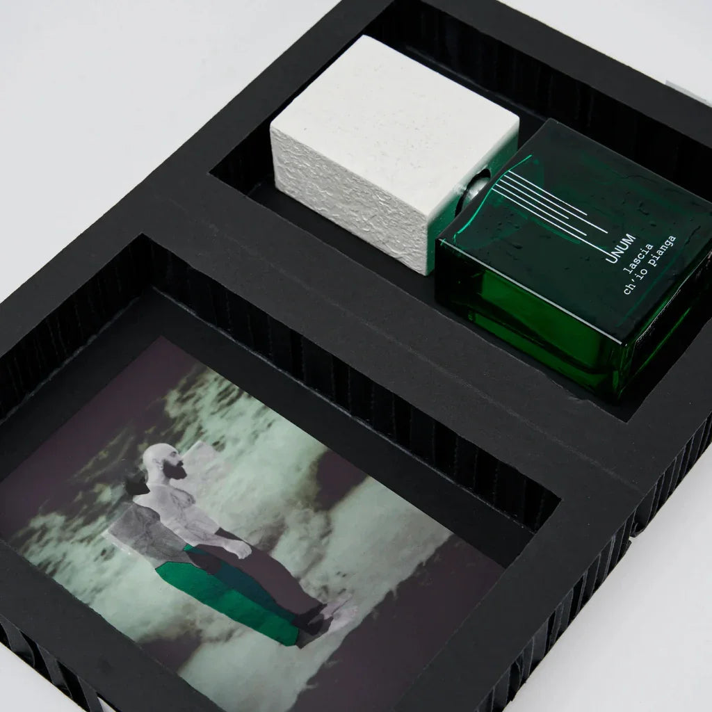 Grüner, quadratischer Parfümflakon "UNUM LASCIA CH´IO PIANGA" von Filippo Sorcinelli, neben einem Kunstfoto in einer Box.