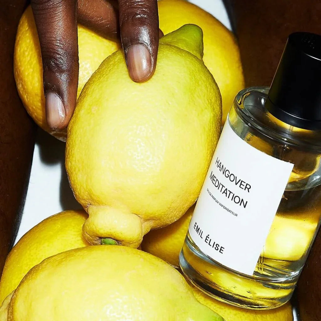 Eine Flasche Parfum mit der Aufschrift "Hangover Meditation" von Emil Élise steht neben mehreren gelben Zitronen.