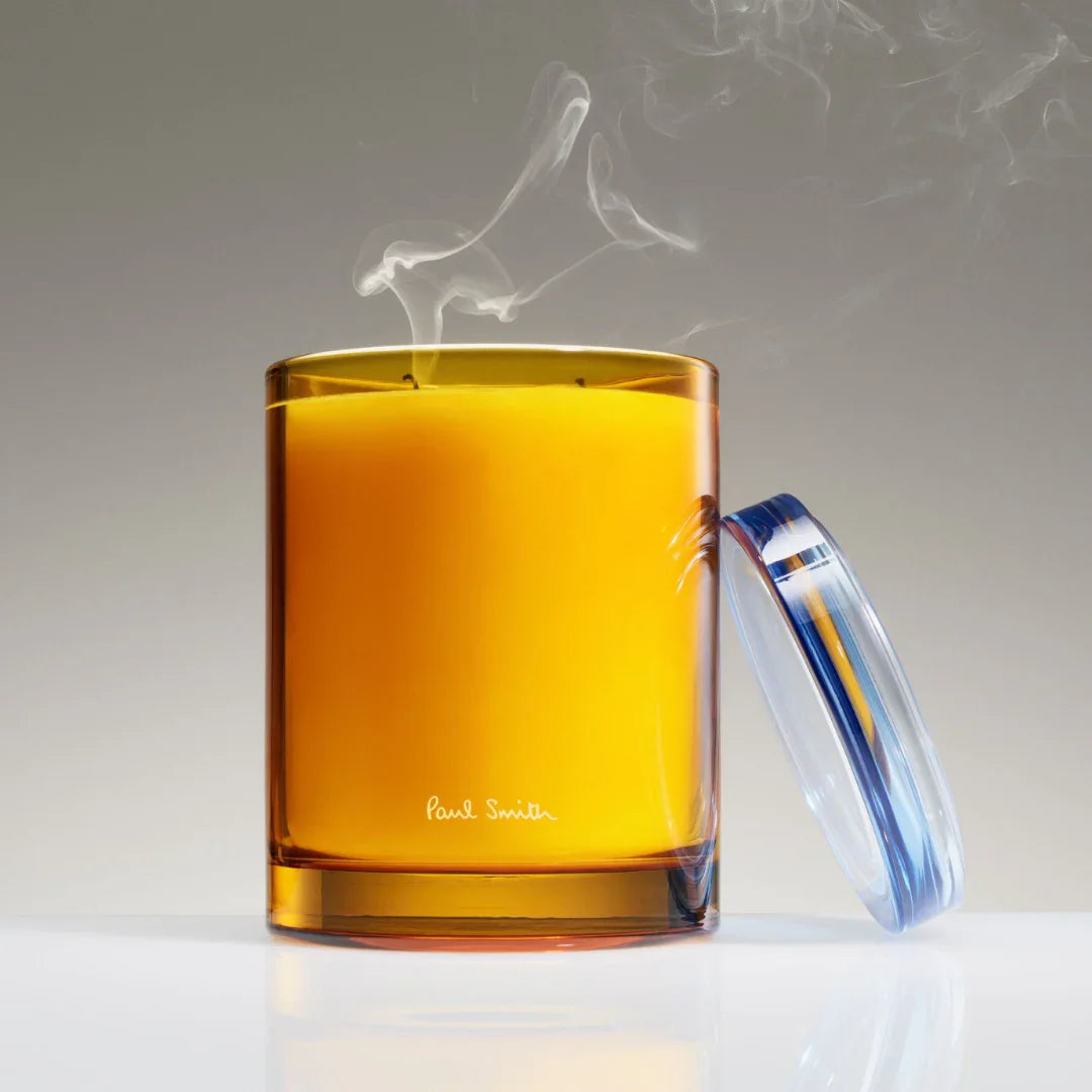 Duftkerze "Day Dreamer" von Paul Smith in einem orangefarbenen Glas mit aufsteigendem Rauch und abgenommener Deckel.