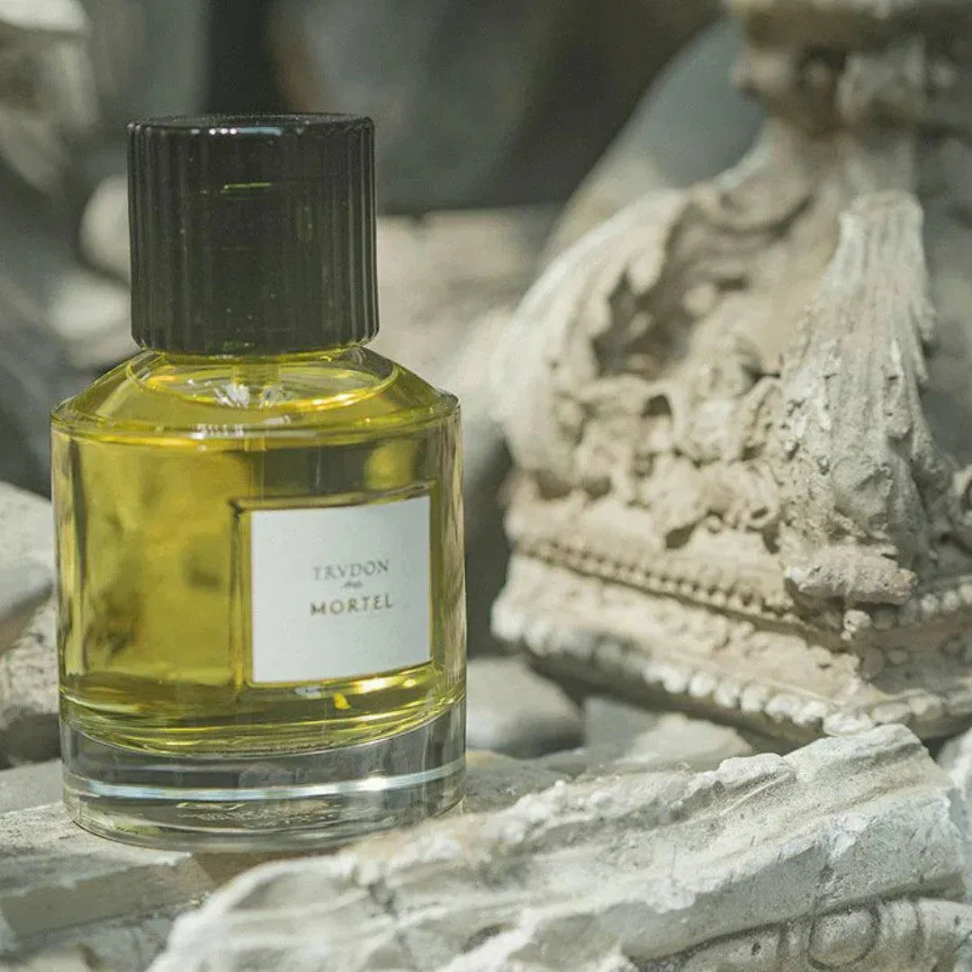Parfümflakon "MORTEL" von Trudon, aus klarem Glas mit schwarzem Verschluss und gelblicher Flüssigkeit.