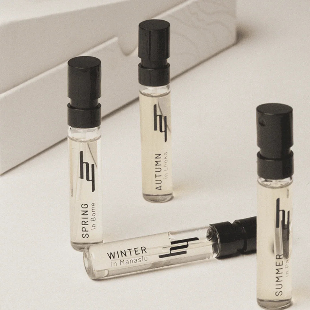 Vier Parfümfläschchen mit schwarzem Sprühkopf, jeweils mit der Aufschrift "SPRING", "AUTUMN", "WINTER", und "SUMMER". Produkt: "Seasons Collection - Discovery Set" von hima jomo.