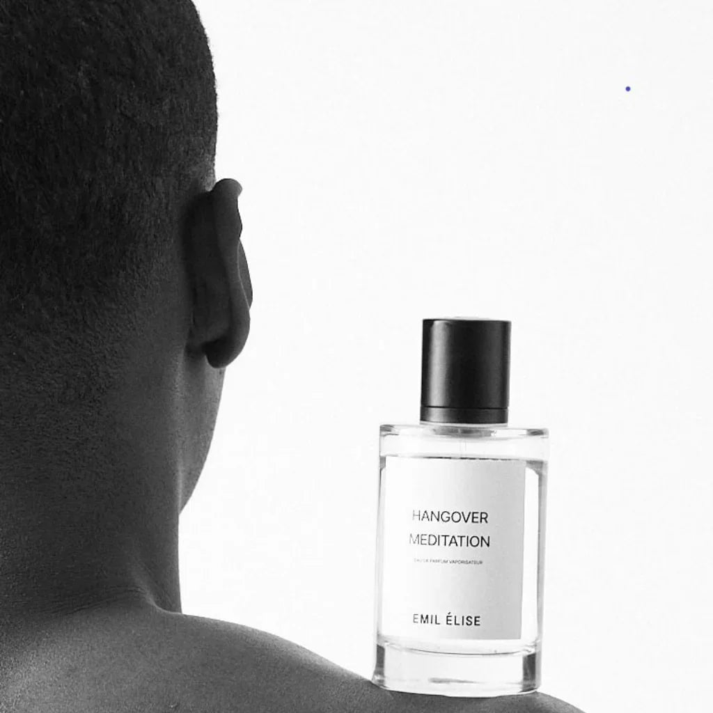Ein Mann hält eine Glassflasche mit schwarzem Deckel. Auf dem Etikett steht "Hangover Meditation" und "Emil Élise".