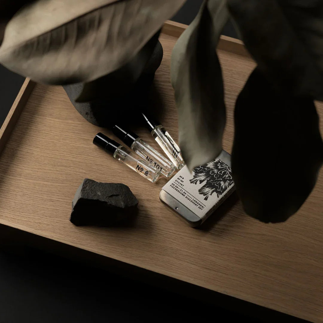 Drei kleine Glasflakons mit der Aufschrift "No 10" und "No 8" liegen auf einem Tablett neben einem schlicht gestalteten Behälter mit floralem Aufdruck. Produkt: Langdegi Discovery Set. Anbieter: Fischersund.