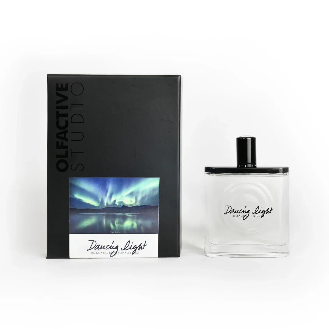 Parfümflasche von "Dancing Light" mit transparentem Glas und schwarzem Verschluss, daneben die Verpackung von Olfactive Studio.