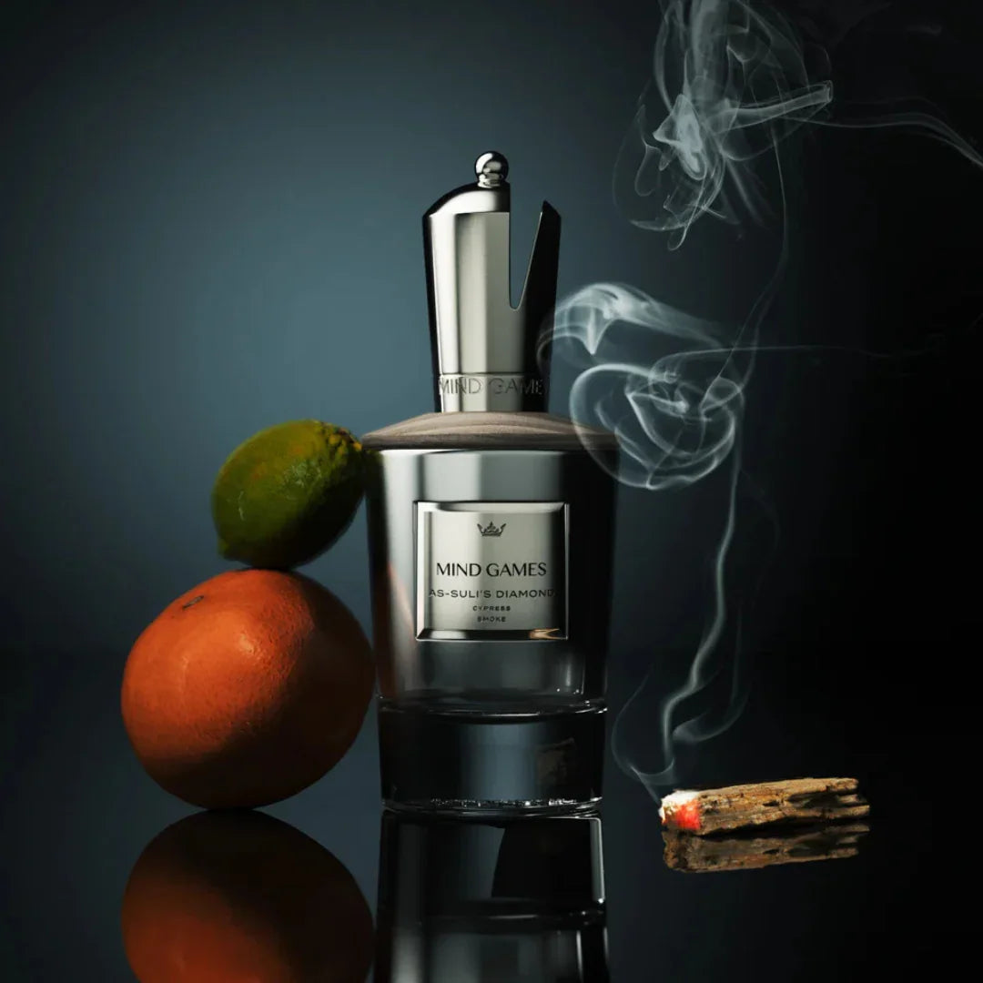 Flakon des Parfums "As-suli's Diamond" von Mind Games, mit silbernem Verschluss, begleitet von Limette, Orange und brennendem Räucherwerk.