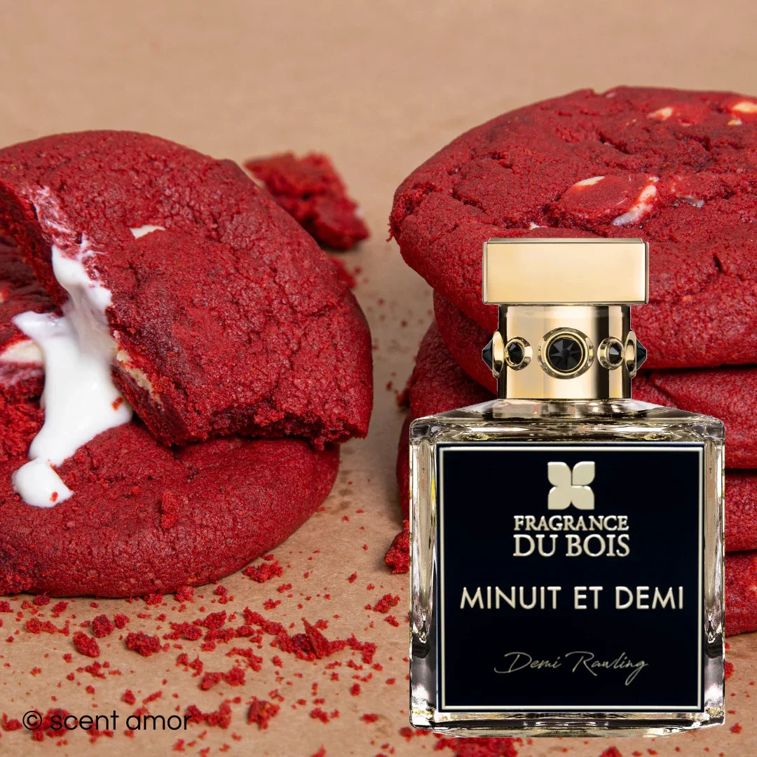 Parfumflasche mit goldener Kappe und schwarzem Etikett vor gestapelten roten Keksen. Produkt: Minuit et Demi von FRAGRANCE DU BOIS.