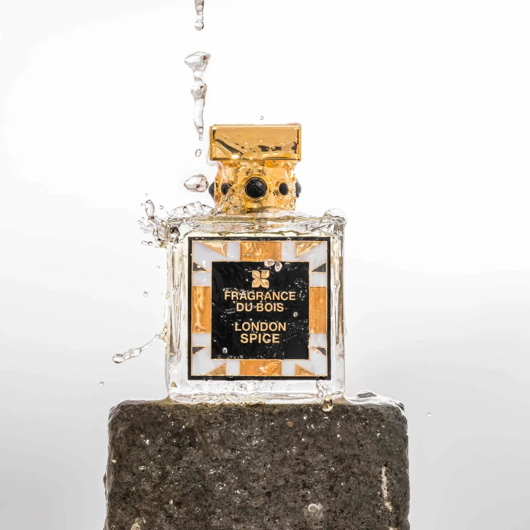 Glasflakon von "London Spice" von "FRAGRANCE DU BOIS" mit schwarzem Etikett und goldfarbenem Verschluss, Wasser spritzt herum.