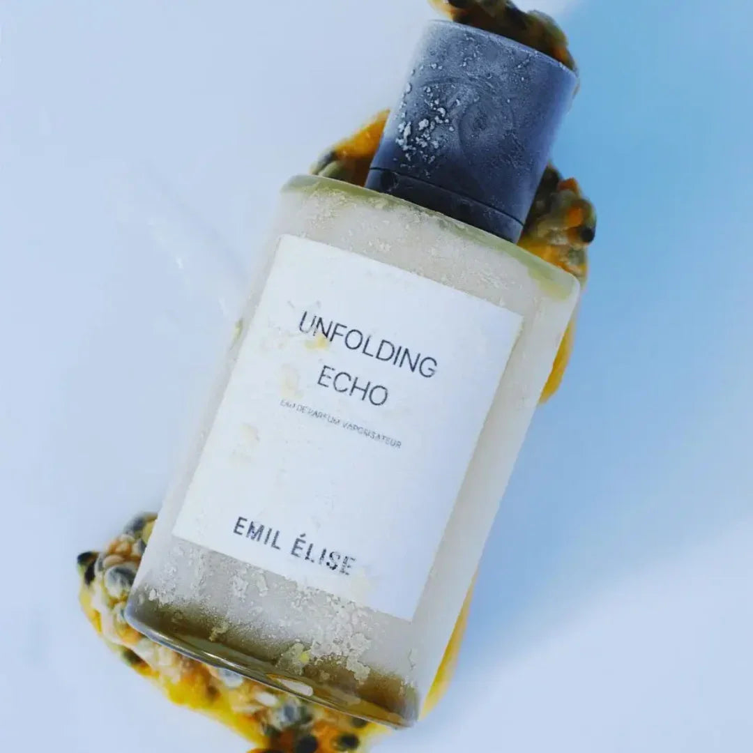 Klare Parfümflasche mit schwarzem Deckel und weißem Etikett, auf dem "Unfolding Echo" von Emil Élise steht.