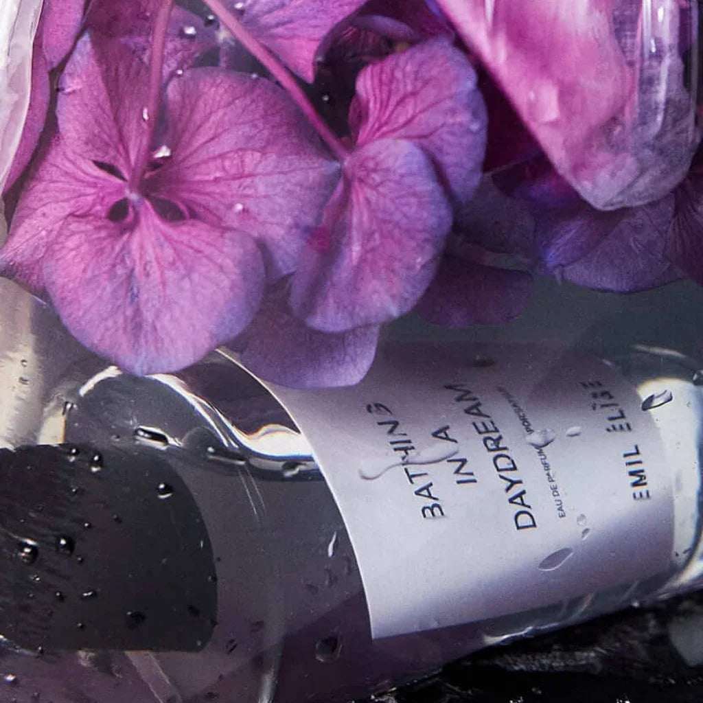 Produkt "Bathing in a Daydream" von Emil Élise, zeigt eine Flasche mit lila Blumen umgeben, Etikett lesbar.