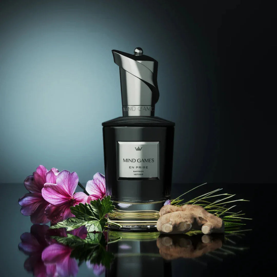 Parfümflakon "En Prise" von Mind Games, mit eleganter Kappe, neben Blüten, Kräutern und Ingwer platziert.