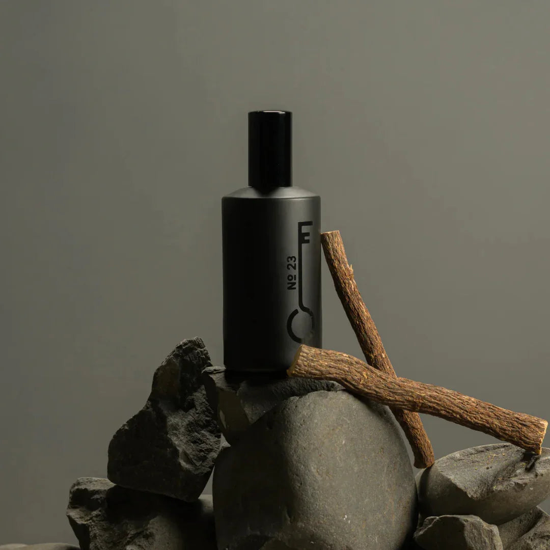 Dunkle, zylindrische Parfümflasche mit der Aufschrift "No. 23" von Fischersund, auf Steinen mit Zweig platziert.