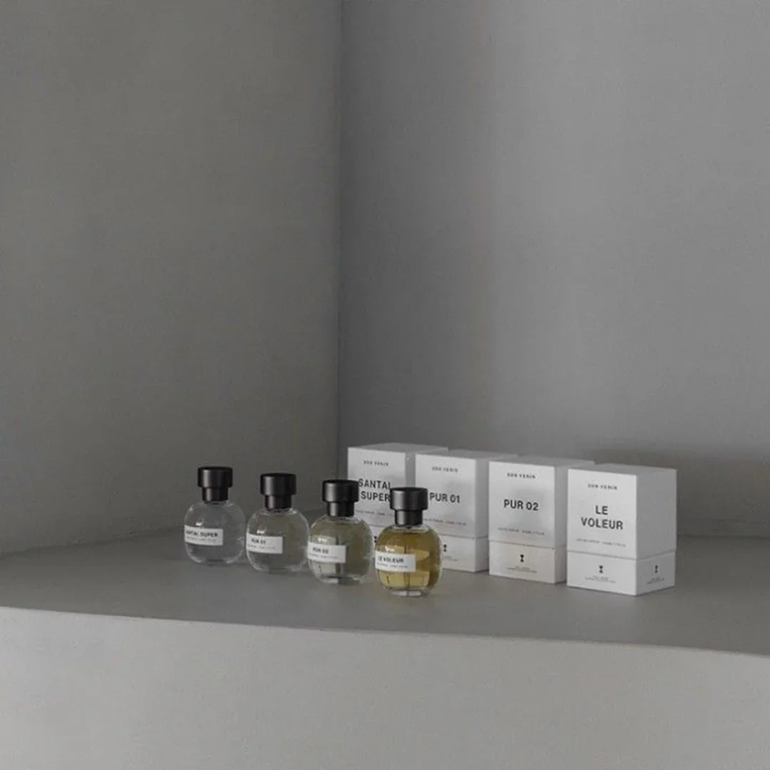 Vier runde Parfümflaschen "Ambr Super" von SON VENÏN mit schwarzen Kappen vor weißen Produktboxen.