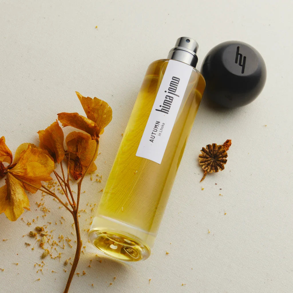 Parfümflasche mit gelbem Duft, Etikett mit "hima jomo" und "AUTUMN in Lhoka". Schwarzer Verschluss liegt daneben.