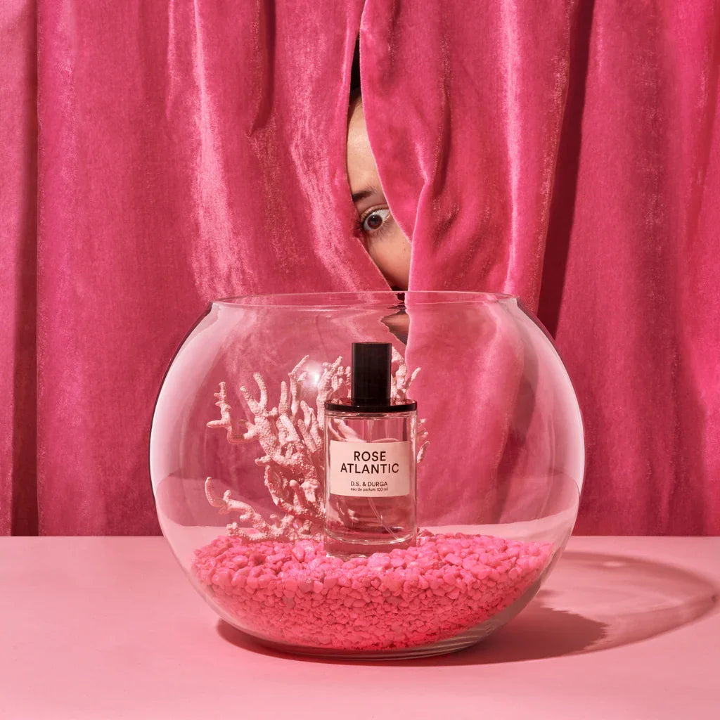 Flasche D.S. & Durga ROSE ATLANTIC Eau de Parfum in einem Glasgefäß mit rosa Dekosteinen und rosafarbenem Vorhang.