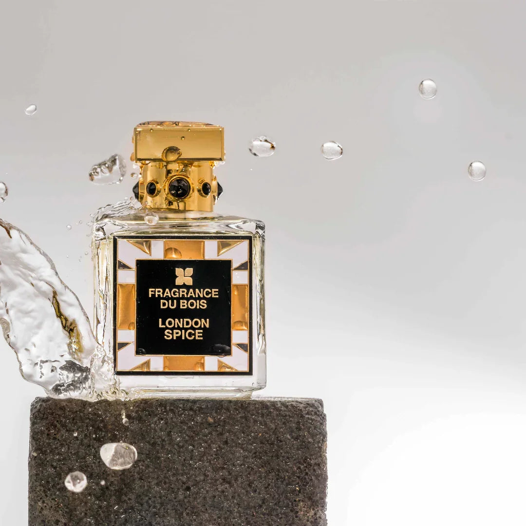 Flasche des Parfums "London Spice" von "FRAGRANCE DU BOIS" mit goldfarbenem Verschluss, stehende auf einem Stein mit Spritzern.