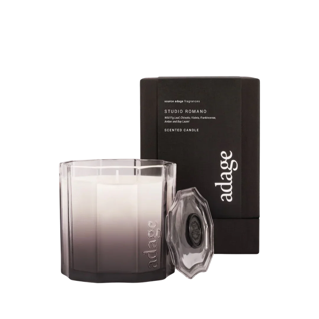 Studio Romano Duftkerze von source adage, mit einem teilweise transparenten Glasbehälter und passendem Deckel, vor einer schwarzen Box.