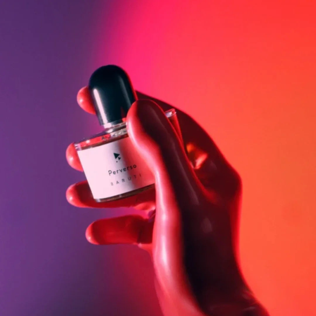 Ein Hand hält ein rundes Parfümflakon mit schwarzem Verschluss, beschriftet mit "Perverso" und "Baruti".