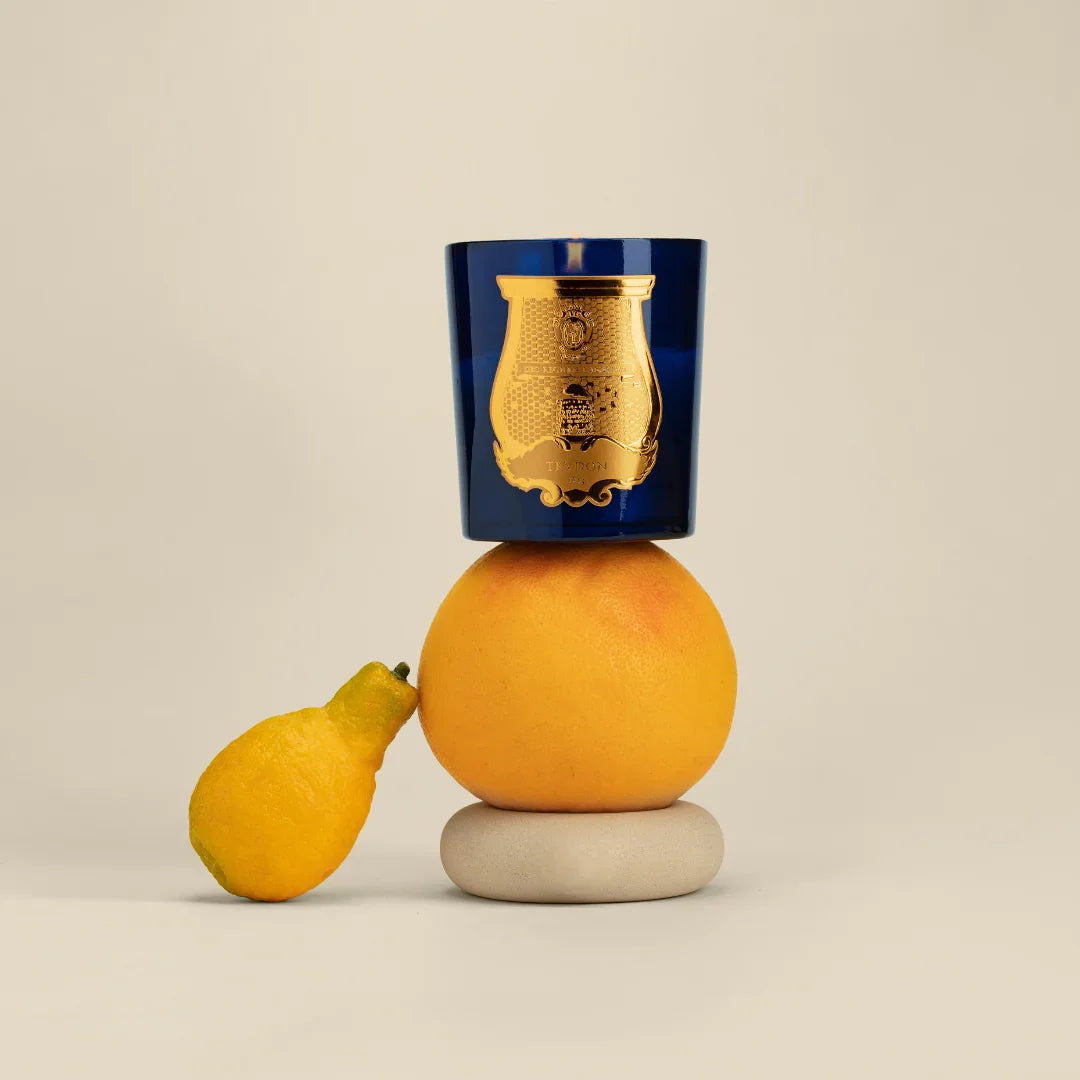Duftkerze "Les Belles Matières - SALTA" von Trudon in einem blauen Glas mit goldener Emblem, neben Zitrusfrüchten.