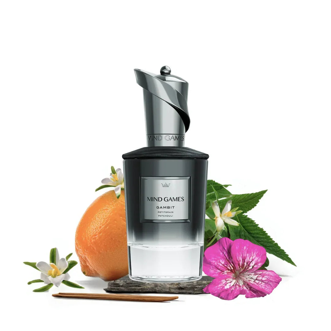 Flasche "Gambit" von Mind Games, schwarze Basis, silberner Verschluss. Umgeben von einer Orange, Blumen und grünen Blättern.