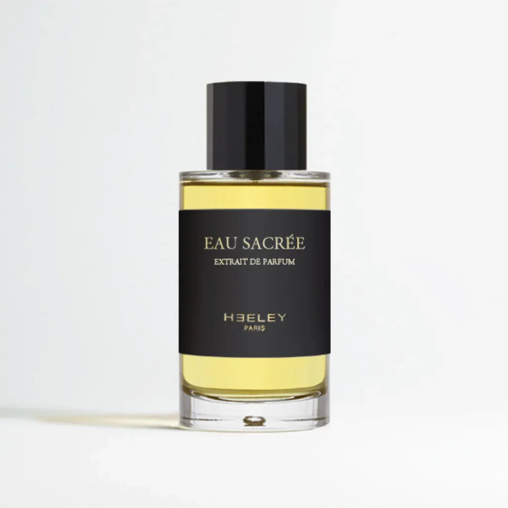 Parfümflakon "Eau Sacrée" von Heeley, zylindrische Form mit schwarzem Etikett auf gelblicher Flüssigkeit.