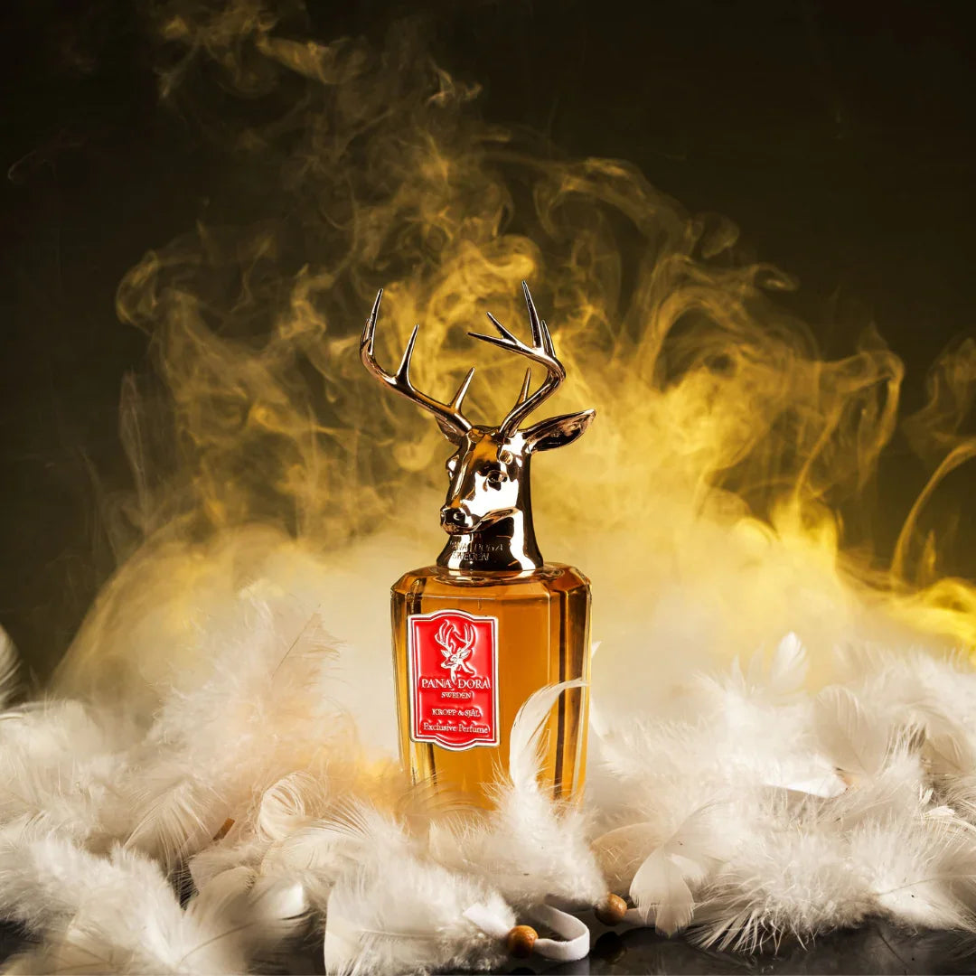 Parfümflasche "Kropp & Själ" von Pana Dora mit Hirschkopf-Verschluss und roten Etikett, umgeben von weißen Federn.