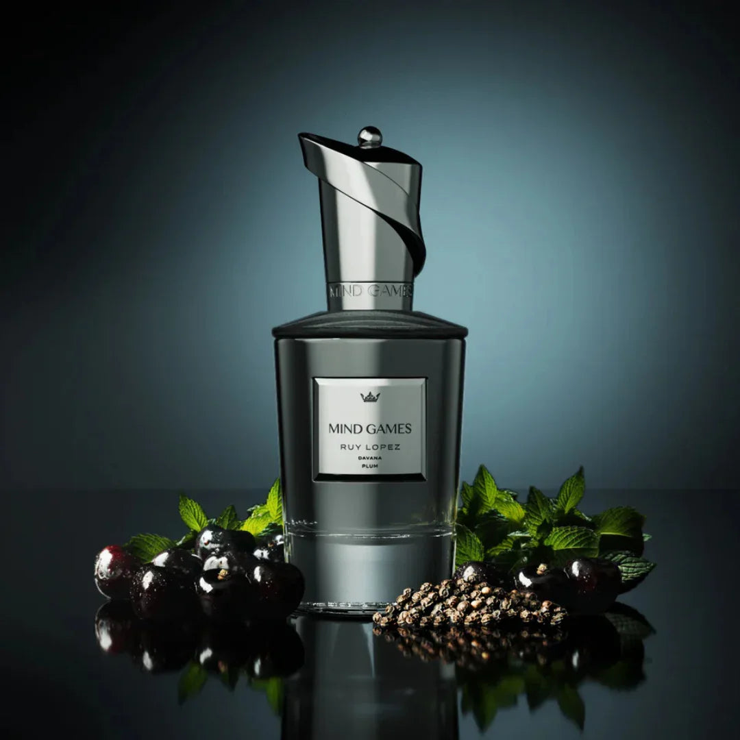 Parfümflakon "Ruy Lopez" von Mind Games aus schwarzem Glas mit silbernen Akzenten, umgeben von Johannisbeeren und Minze.