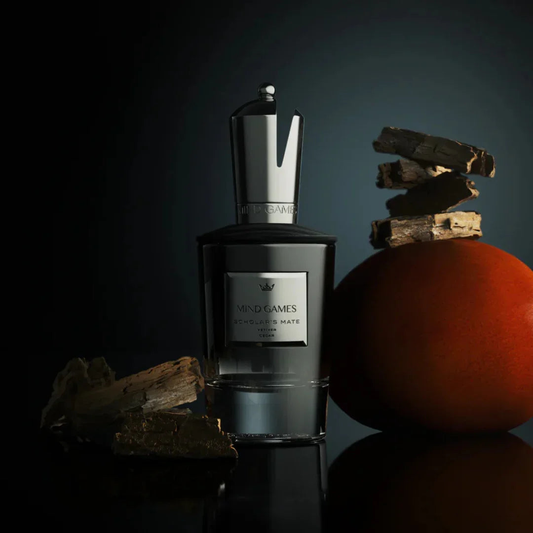 Parfümflasche "Scholar's Mate" von Mind Games, mit silberner Kappe; daneben Barkstücken und eine orangefarbene Kugel.