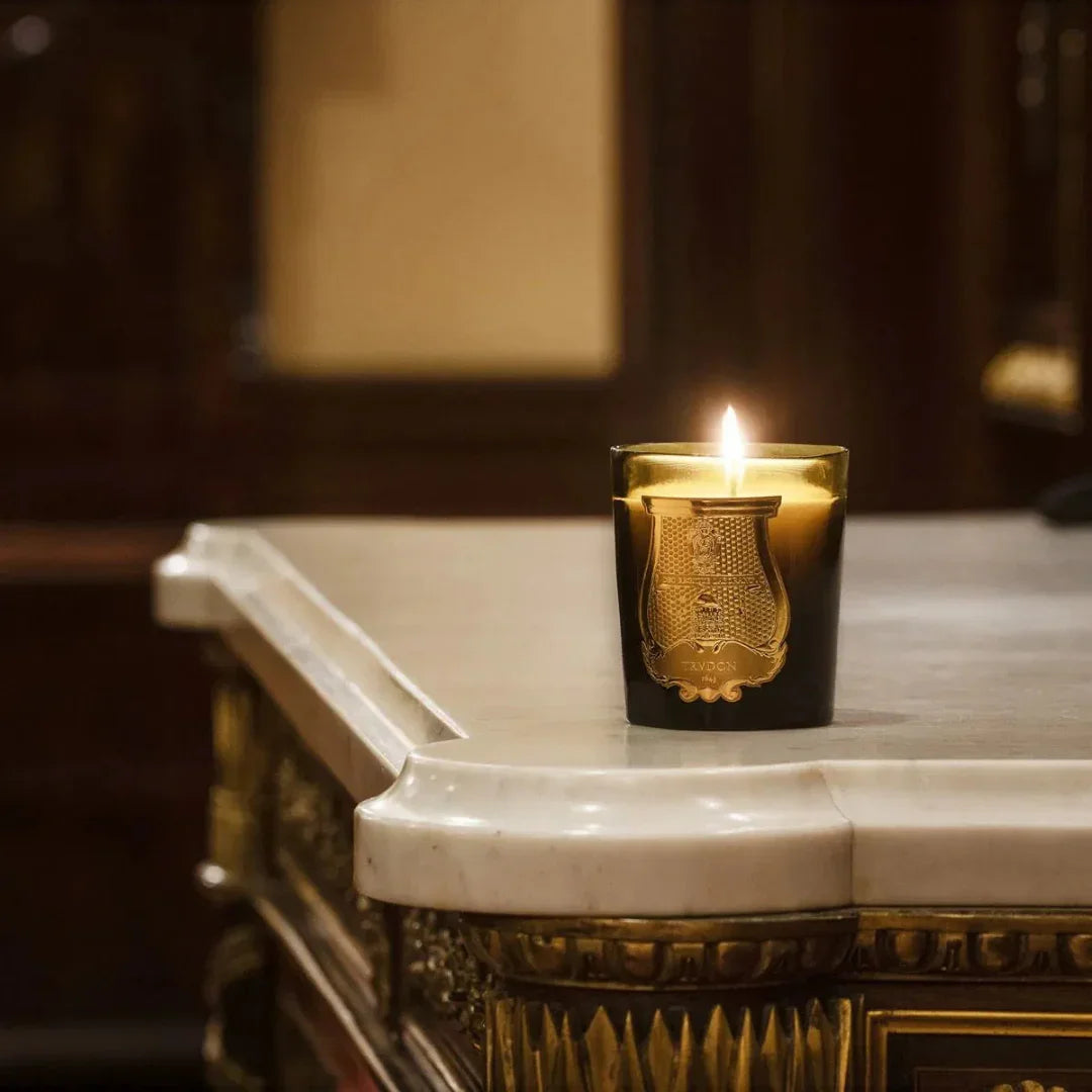 Duftkerze "ODALISQUE" von Trudon auf einem dekorativ geschnitzten Tisch. Die Kerze brennt in einem dunkelgrünen Glasgefäß.