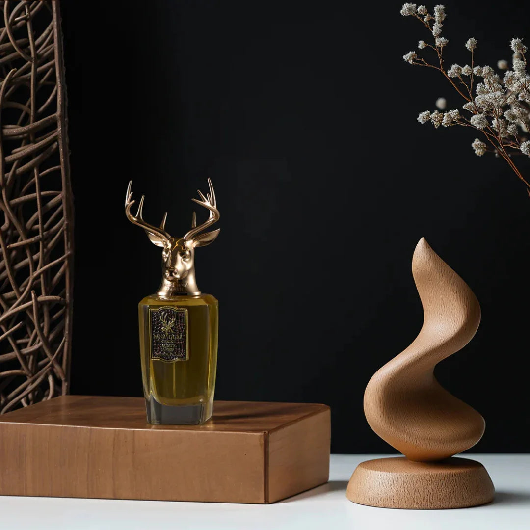 Parfümflakon "Majestic Amber" von Pana Dora mit Hirschkopf-Verschluss auf Holzblock, neben kunstvoller Holzskulptur.