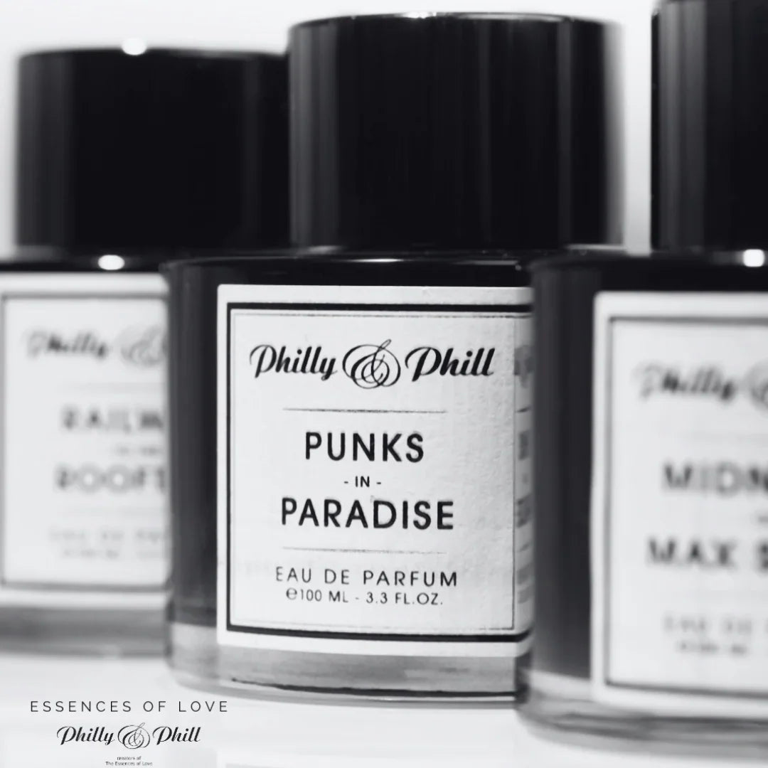 Drei Parfumflaschen mit runden schwarzen Kappen und etikettiert mit "PUNKS IN PARADISE" von Philly & Phill.
