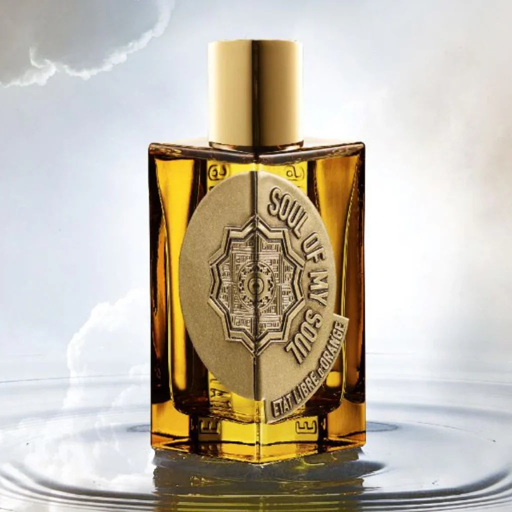 Parfümflasche mit rechteckigem Glasflakon, gefüllt mit goldener Flüssigkeit. Auf der Vorderseite ein großes, rundes goldenes Emblem mit "SOUL OF MY SOUL" und "ETAT LIBRE D'ORANGE". Produkt: Soul of my Soul, Anbieter: Etat Libre D'Orange.