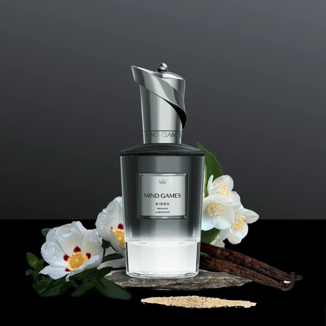 Parfümflakon "Sissa" von Mind Games mit transparentem Glas, eleganter silberner Kappe und Blumen im Hintergrund.