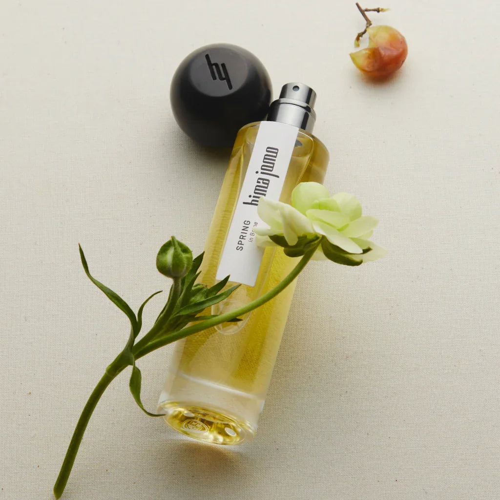 Parfümflasche mit gelblicher Flüssigkeit, schwarzem Sprühkopf und weißem Etikett "hima jomo". Titel: "Seasons Collection - Spring in Bome", Anbieter: hima jomo.