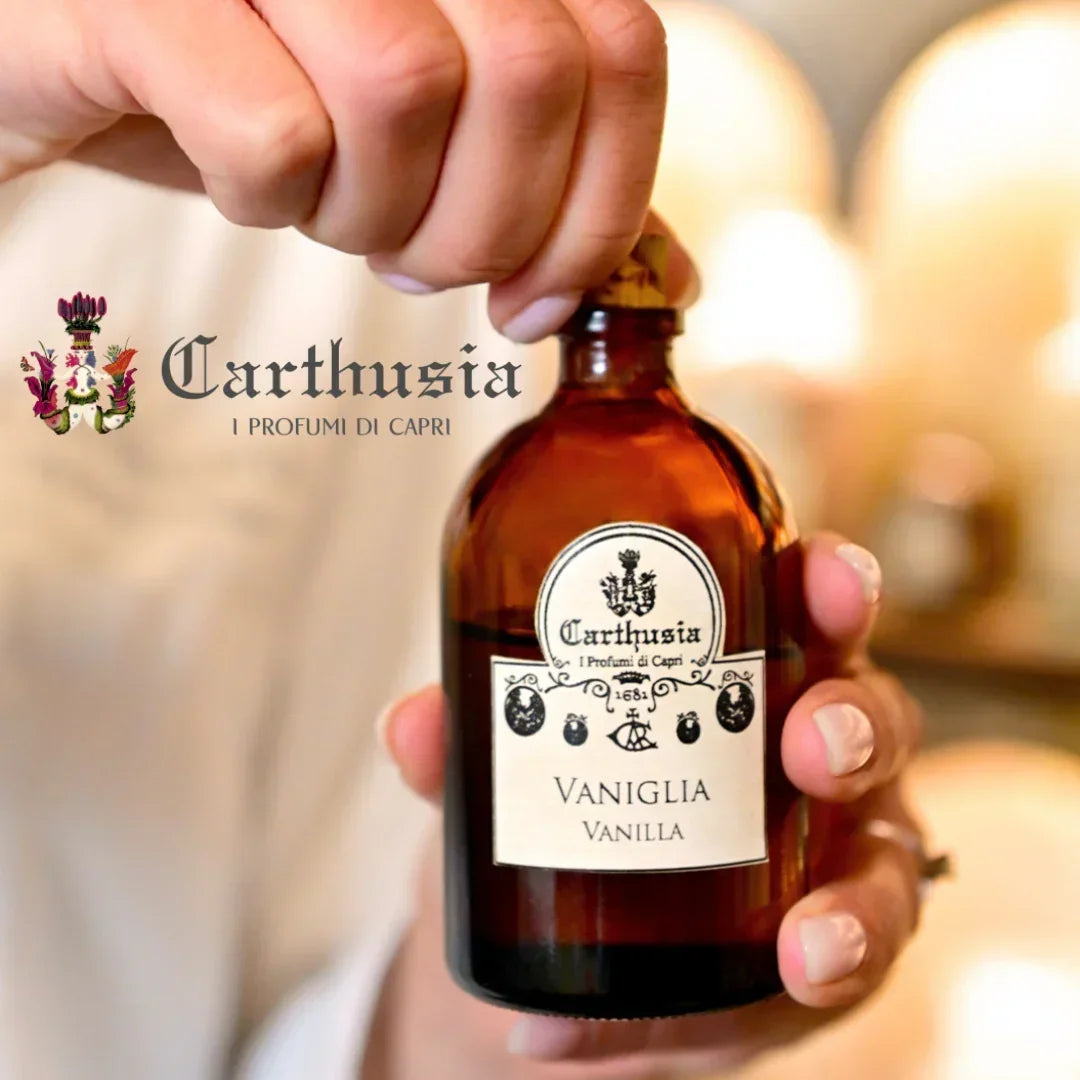 Carthusia Mediterraneo Diffuser: Eine Hand hält eine braune Glasflasche mit "Vaniglia Vanilla" Etikett. "Carthusia" Logo oben.