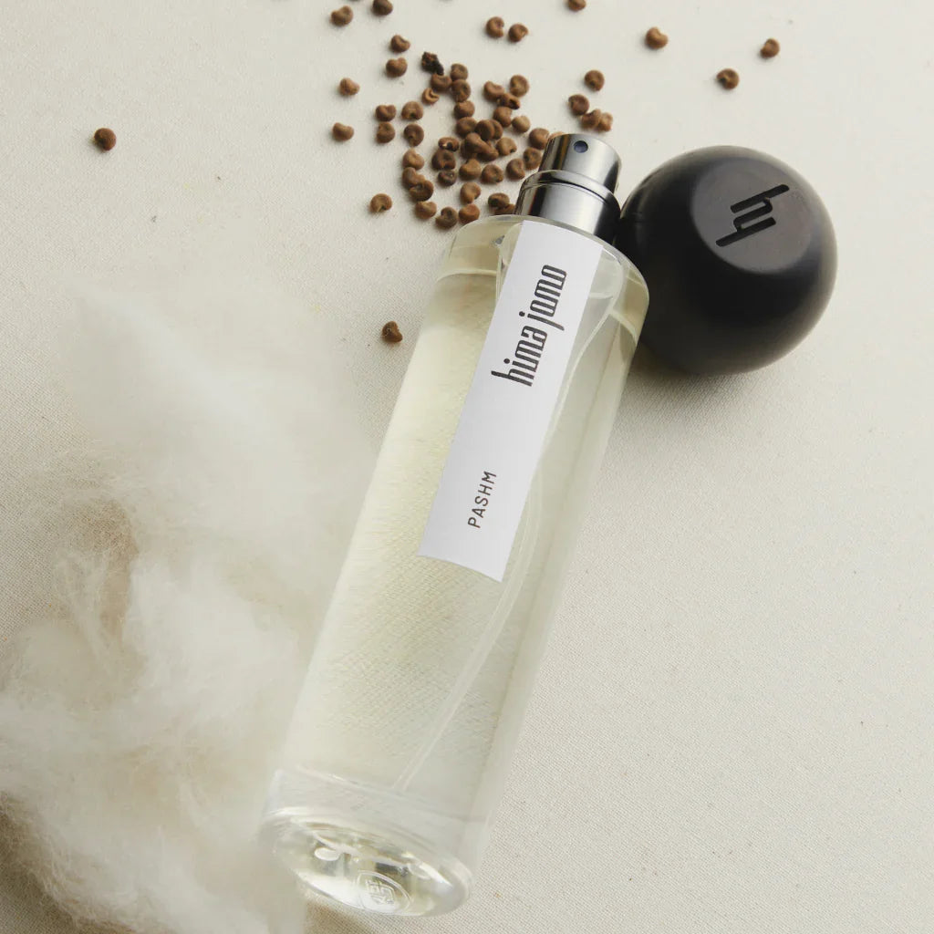 Parfümflasche "Treasure Collection - Pashm" von hima jomo. Transparente Glasflasche mit schwarzer Kappe und Etikett.