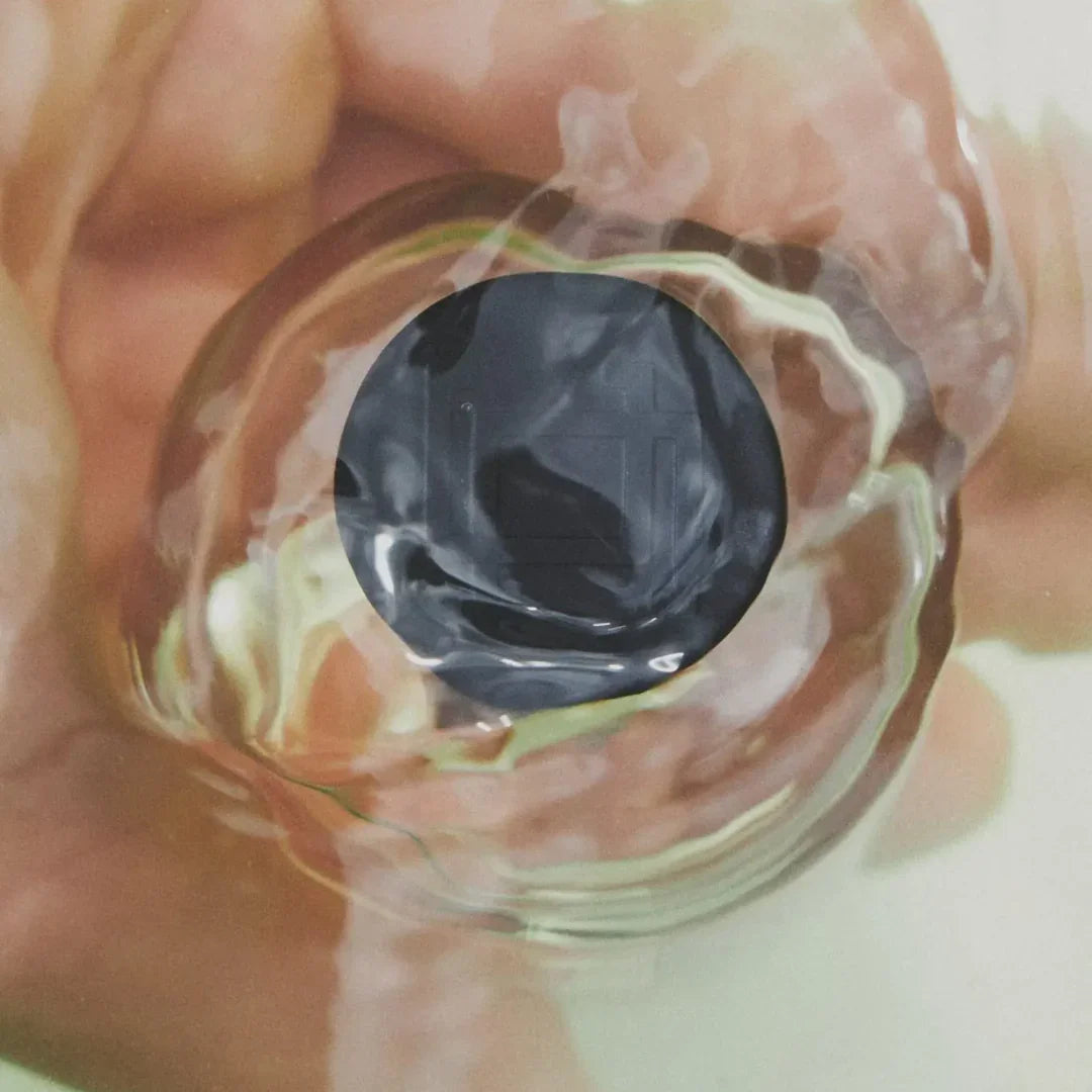 Nahaufnahme eines runden, dunklen Flakons mit einem welligen Glasrand. Produkt: Unfolding Echo von Emil Élise.