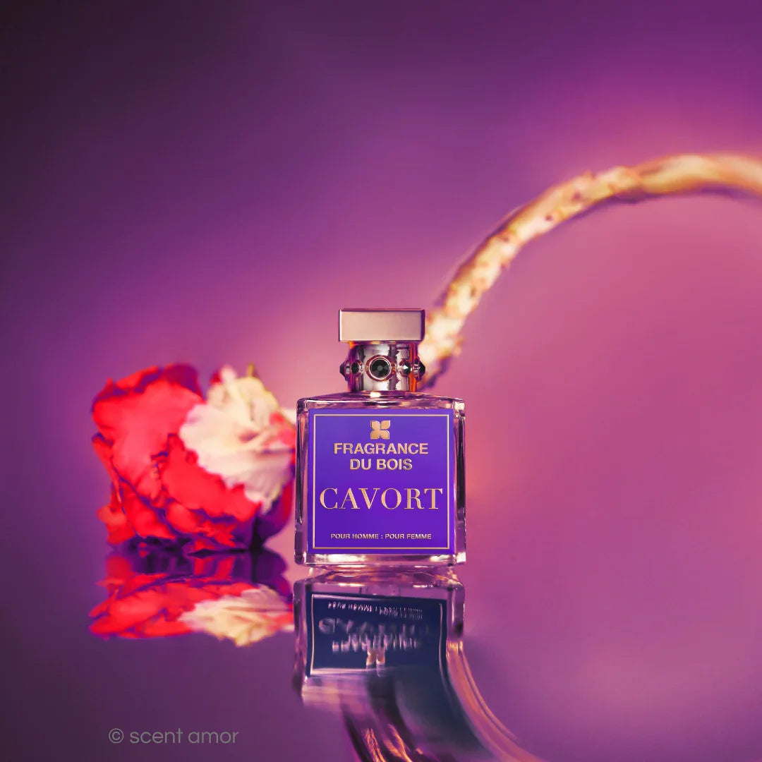 Parfümflakon "Cavort" von FRAGRANCE DU BOIS, mit violettem Etikett, neben einer roten Blume auf spiegelnder Oberfläche.