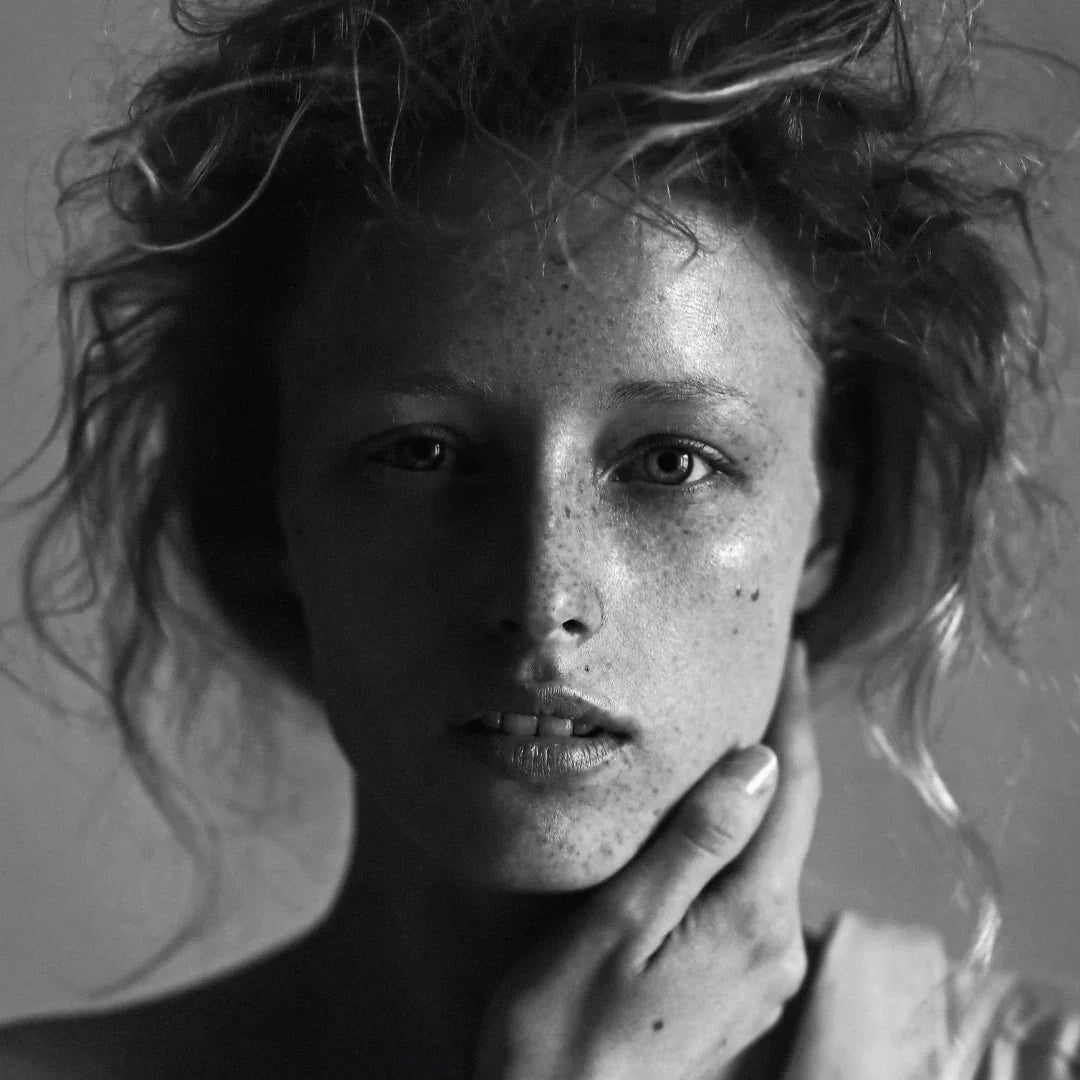 Schwarz-weiß-Porträtfoto einer Person mit lockigem Haar, die das Gesicht berührt. Produkt: Peligroso, Anbieter: FUMparFUM.