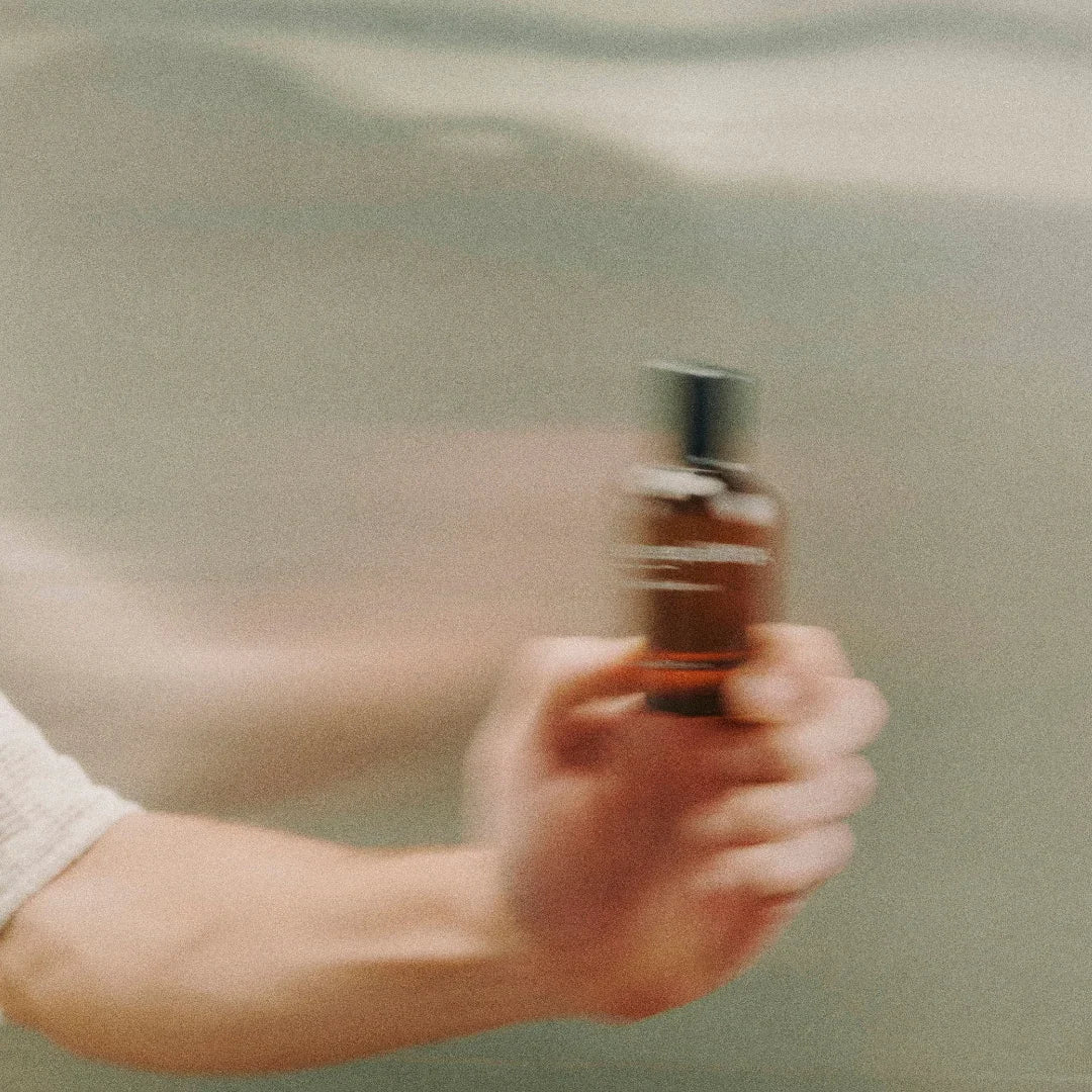 Eine Hand hält eine braune Sprühflasche mit schwarzem Verschluss. Titel: equality, Anbieter: equality.