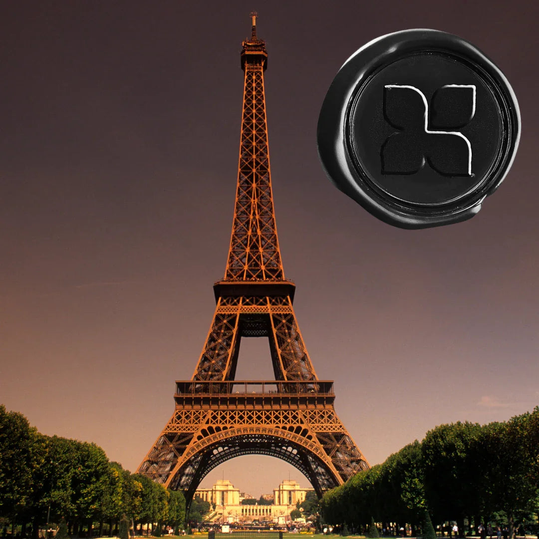 Der Duft "Voyage à Paris" von FRAGRANCE DU BOIS zeigt den Eiffelturm und ein rundes, schwarzes Siegel mit einem Relief.