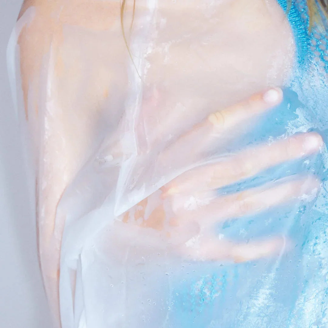 Nahaufnahme eines transparenten Stoffes, der über eine Hand und ein Kleidungsstück in Blau drapiert ist. Produkt: Bathing in a Daydream, Anbieter: Emil Élise.